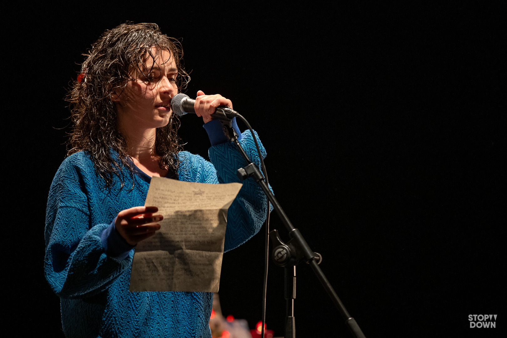 Brixhilda Shqualsi attrice legge al microfono da un foglio che tiene in mano sul palco nello spettacolo Il tempo che abbiamo perso. Ph Giorgio Prodoti