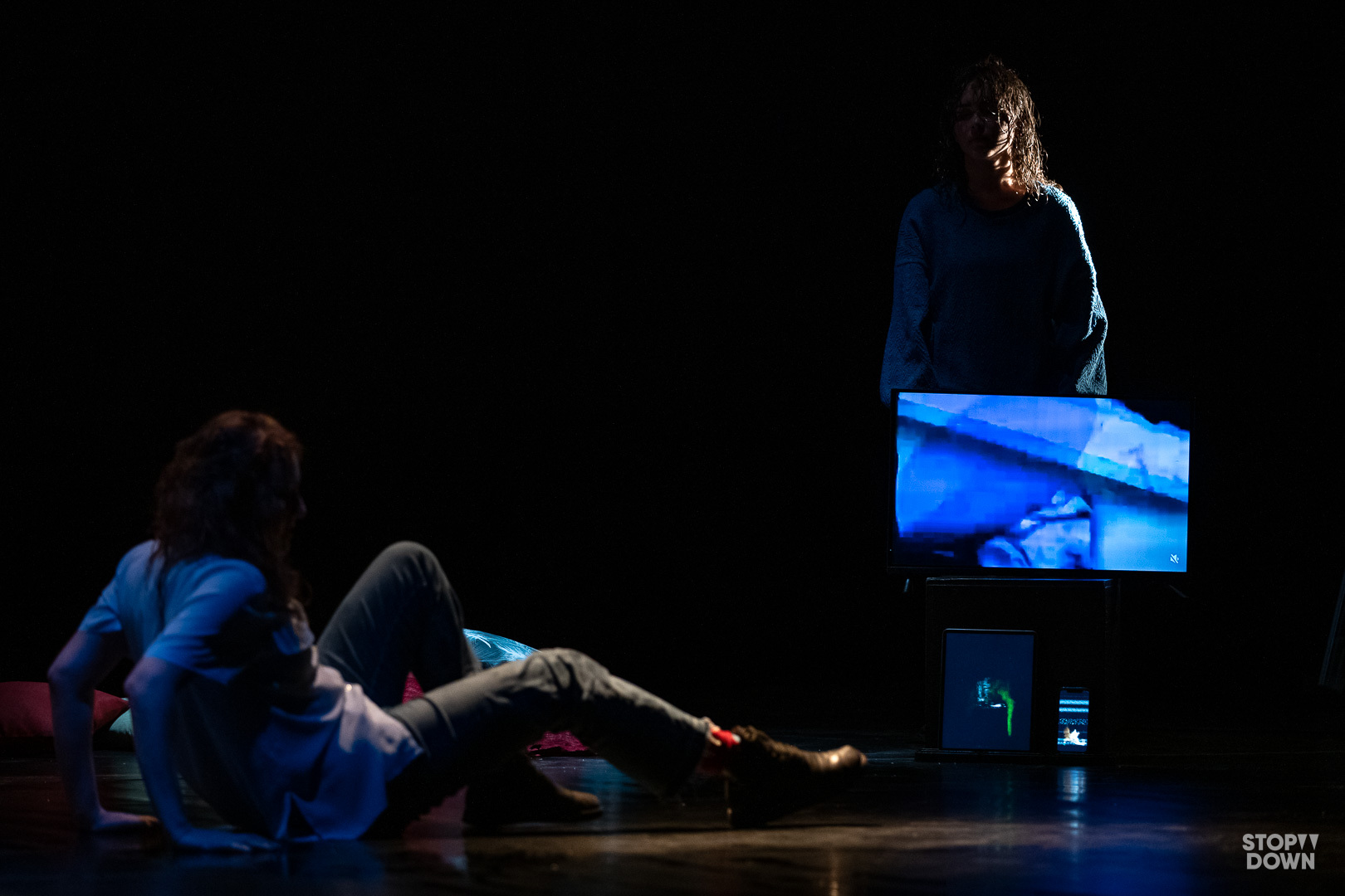 Andrea Cazzato e Brixhilda Shqualsi recitano sul palco, uno sdraiato l'altra in piedi sorregge uno schermo blu nella performance Il tempo che abbiamo perso. Ph Giorgio Prodoti
