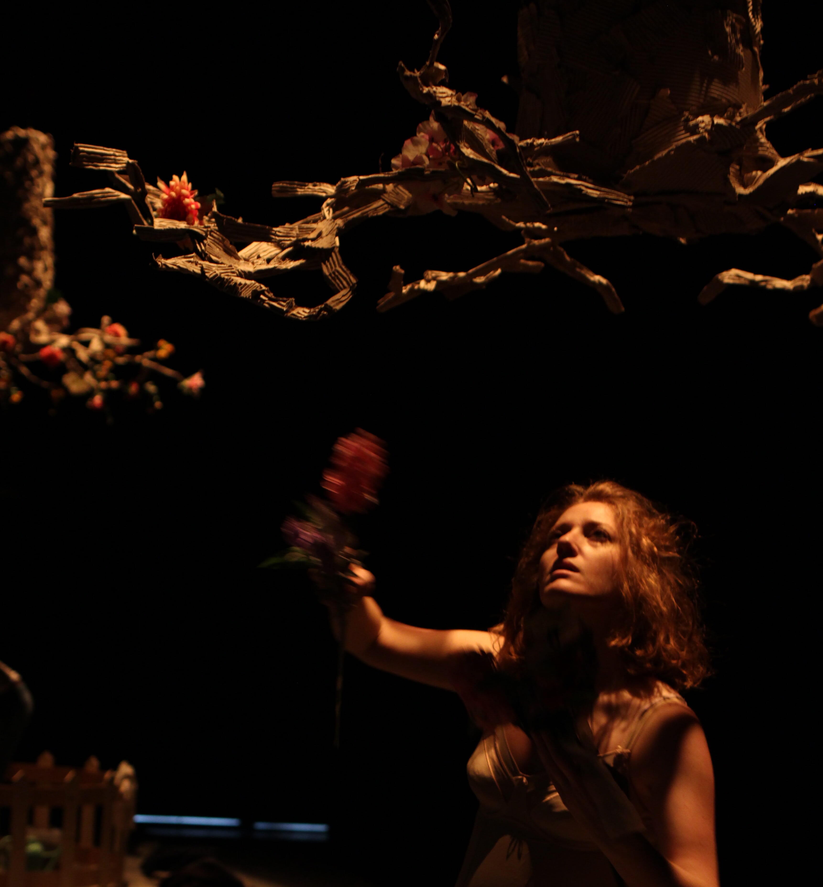 Stefania Tagliaferri attrice recita nello spettacolo di Palinodie: Bian o la teoria dei barattoli. Ha il viso rivolto verso l'alto, ai rami di un albero finto appeso capolvolto. Nella mano destra un fiore finto colorato.