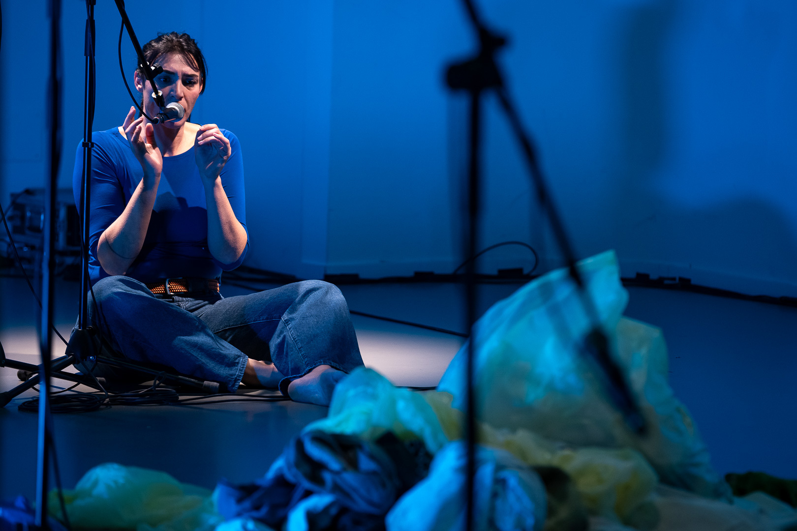 Attrice Silvia Pietta seduta in secondo piano e sta recitando al microfono nello spettacolo sulla violenza donne Come noi. Fotografo Stopdown