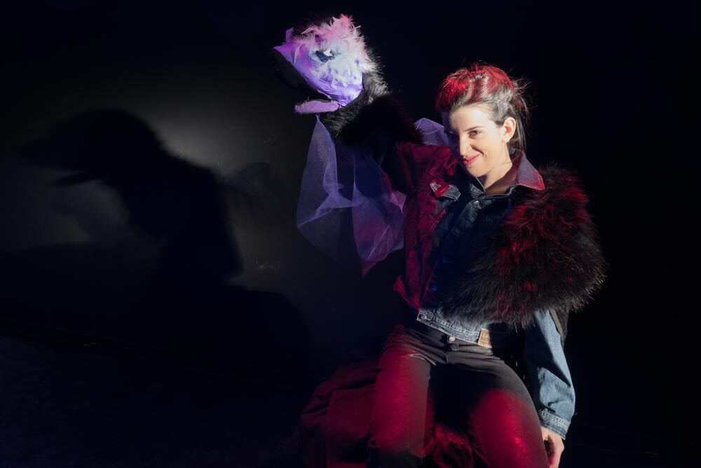 Francesca Zanin attrice in primo piano mentre recita in ginocchio sorridendo e sollevando la mano destra, dalle fattezze di testa di drago, parte del costume di scena che sta indossando per lo spettacolo Un racconto di draghi.